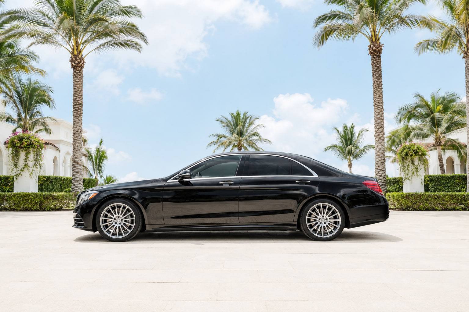 Black luxury sedan parked under tall palms at a South Florida estate